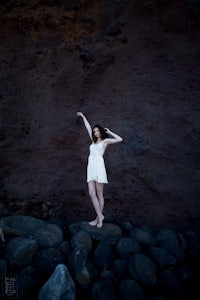 a girl in a white dress standing on rocks in front of a rock wall