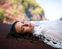 a woman in a white dress laying on a red sand beach